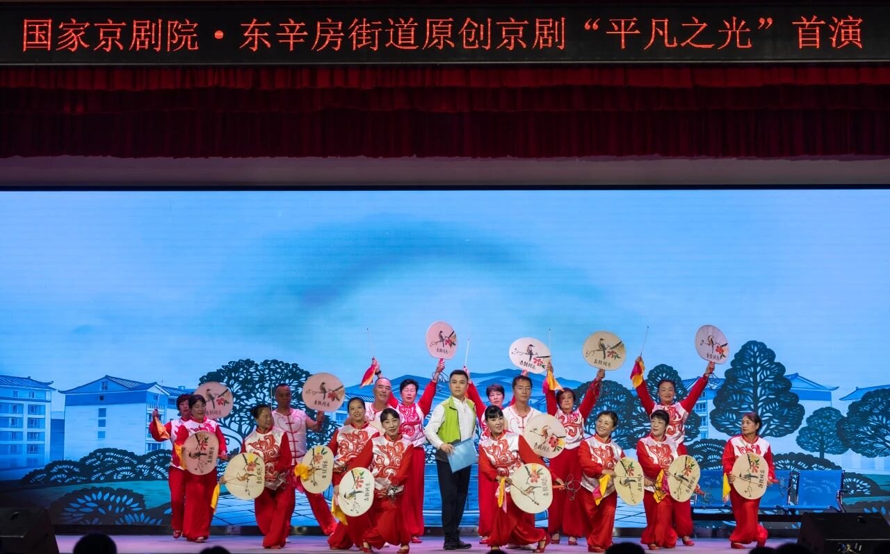 原创京剧《平凡之光》首演:东辛房街道居民与群众文艺队伍登台(台口横幅可辨「国家京剧院·东辛房街道原创京剧《平凡之光》首演」)