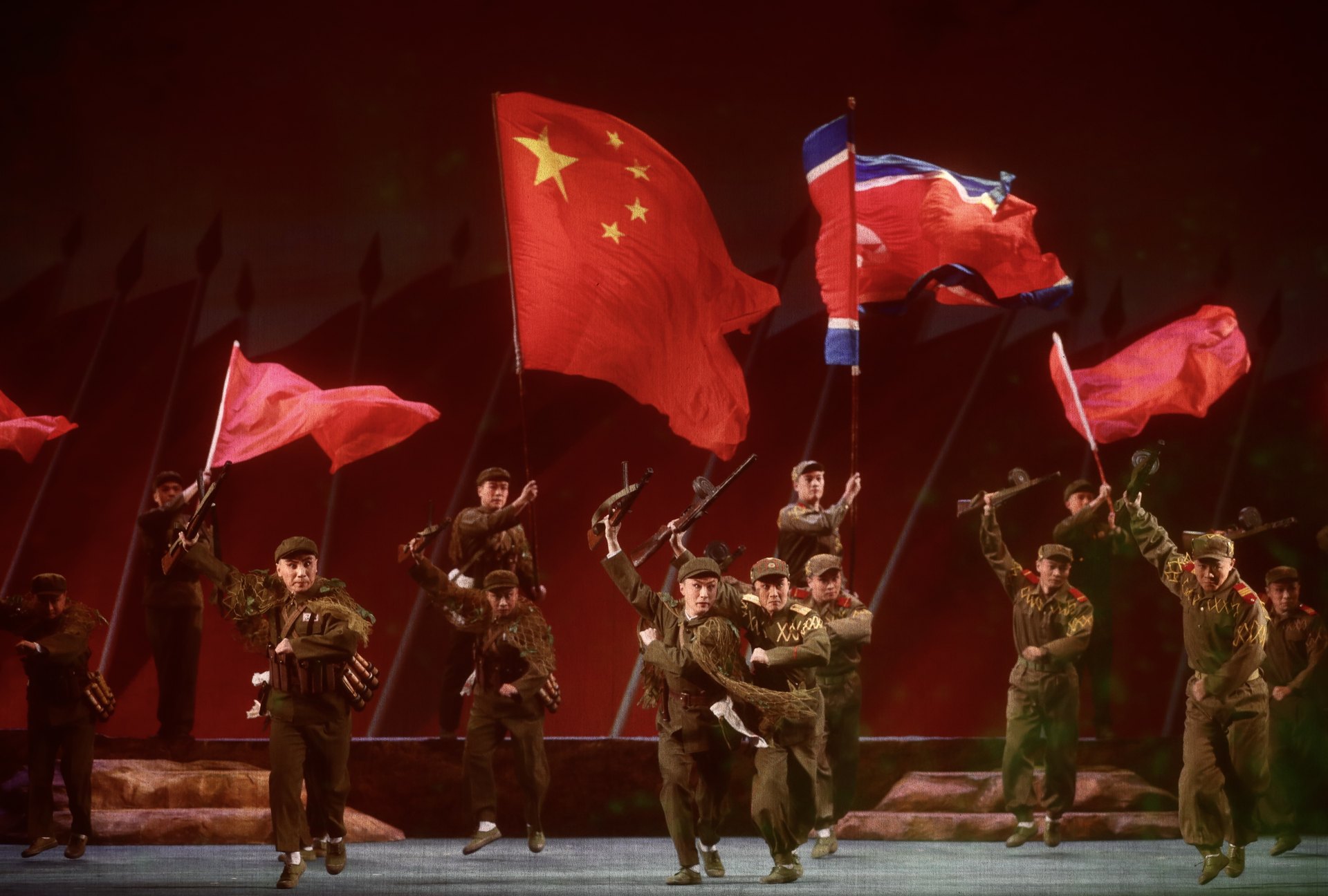 现代京剧《奇袭白虎团》剧照:中国人民志愿军战士持枪群像与中朝两国国旗(2020年纪念中国人民志愿军抗美援朝出国作战70周年舞台艺术优秀剧目展演开幕演出)
