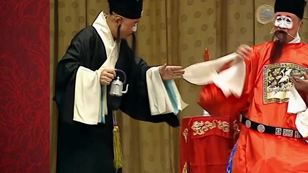京剧《审头刺汤》「审头」公堂录像截帧:老生(左)与汤勤(丑,右,白面红官衣)当堂对白
