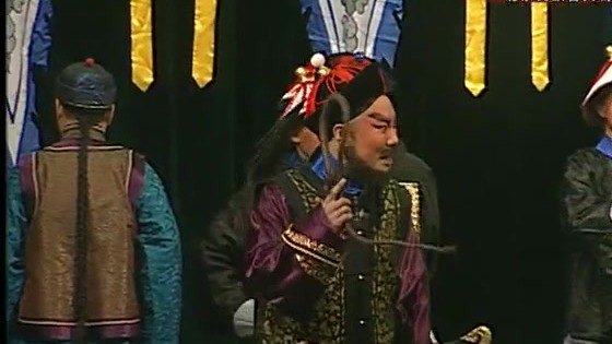 京剧《廉吏于成龙》演出照:公堂/官场场面——官服人物居中,差役背身侍立,台口悬蓝黄旗帜