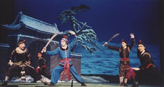 京剧《野猪林》剧照:雪夜覆雪山门与雪地松树,林冲(武生俊扮)持刀与众角色开打(国家京剧院官网剧目页所载)